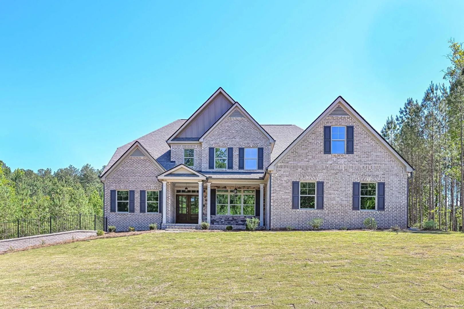 Two-story brick home with gray roof and shutters, green lawn, and trees under a blue sky.