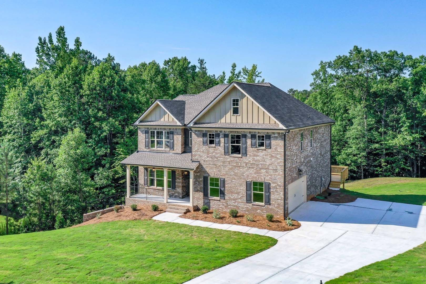 Two-story brick home with a driveway, green lawn, and surrounded by trees under a blue sky.