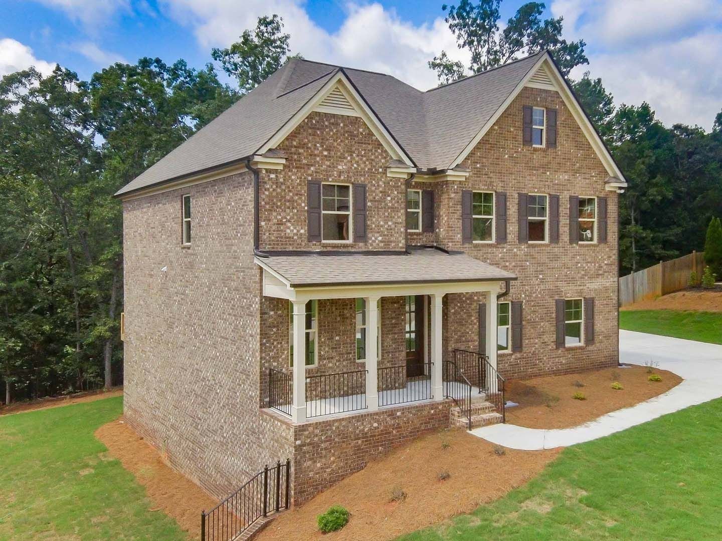 Two-story brick house with porch and dark shutters; surrounded by green grass and trees.