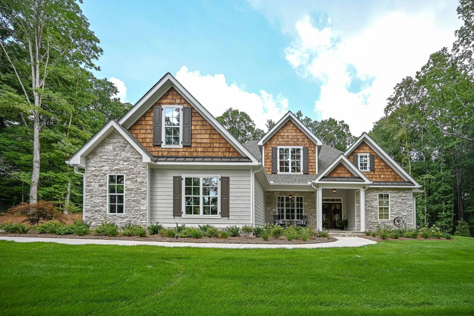 Ranch-style house with stone and wood siding, set on a green lawn, surrounded by trees on a sunny day.
