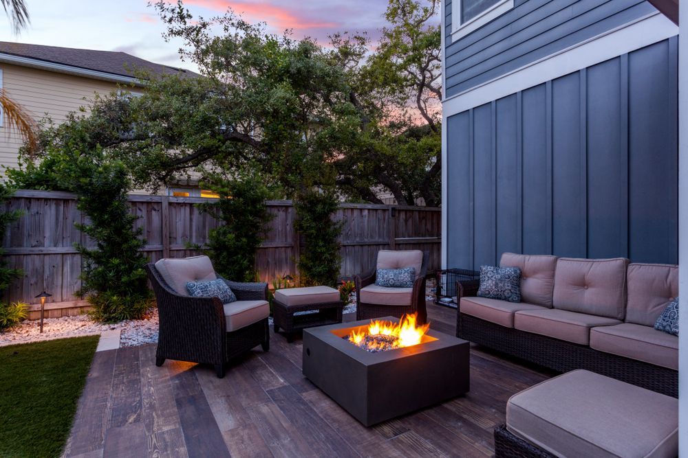 Outdoor patio with lit fire pit, seating, wooden flooring, and evening sky.