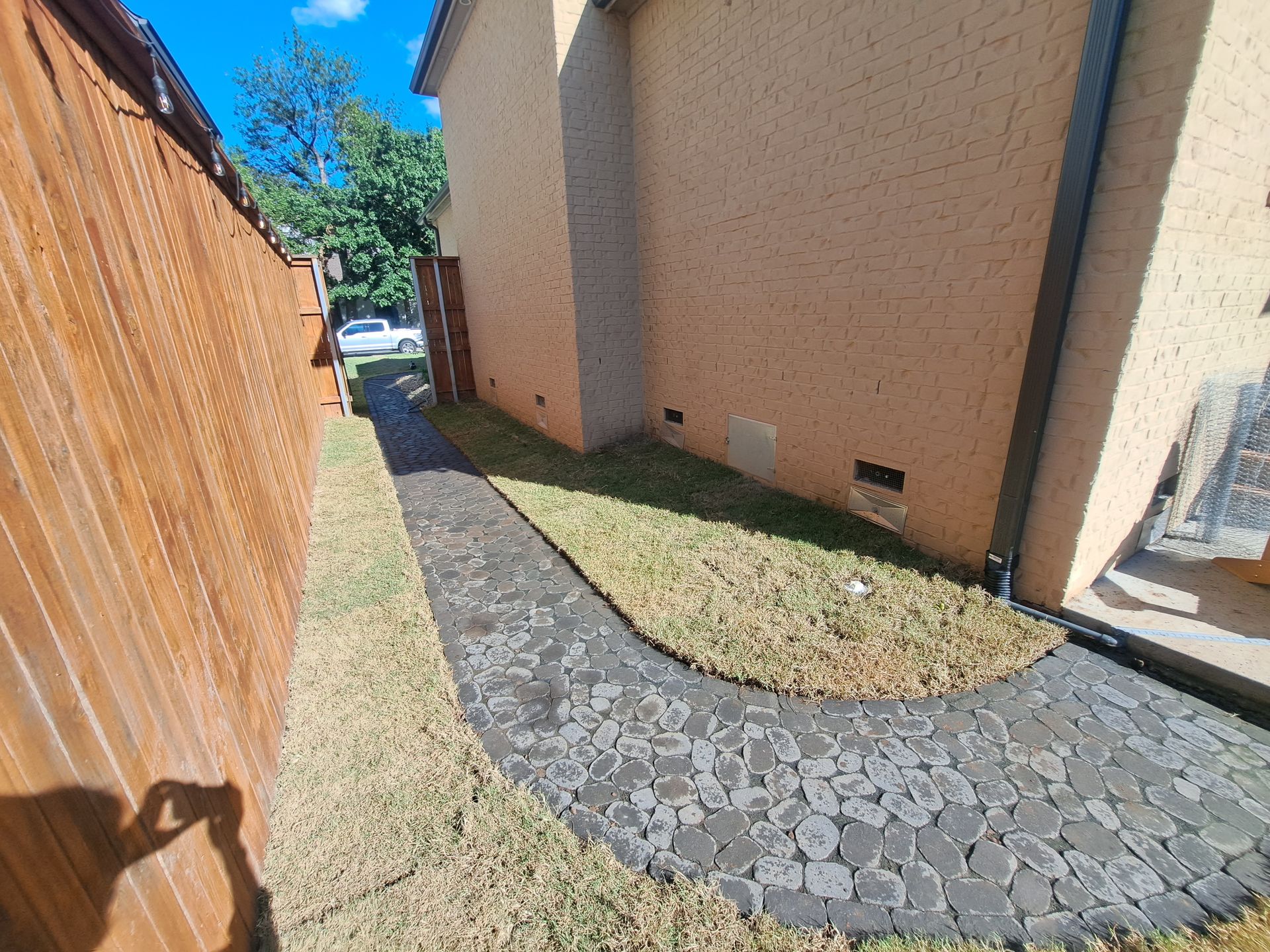 A sidewalk leading to a house next to a wooden fence.