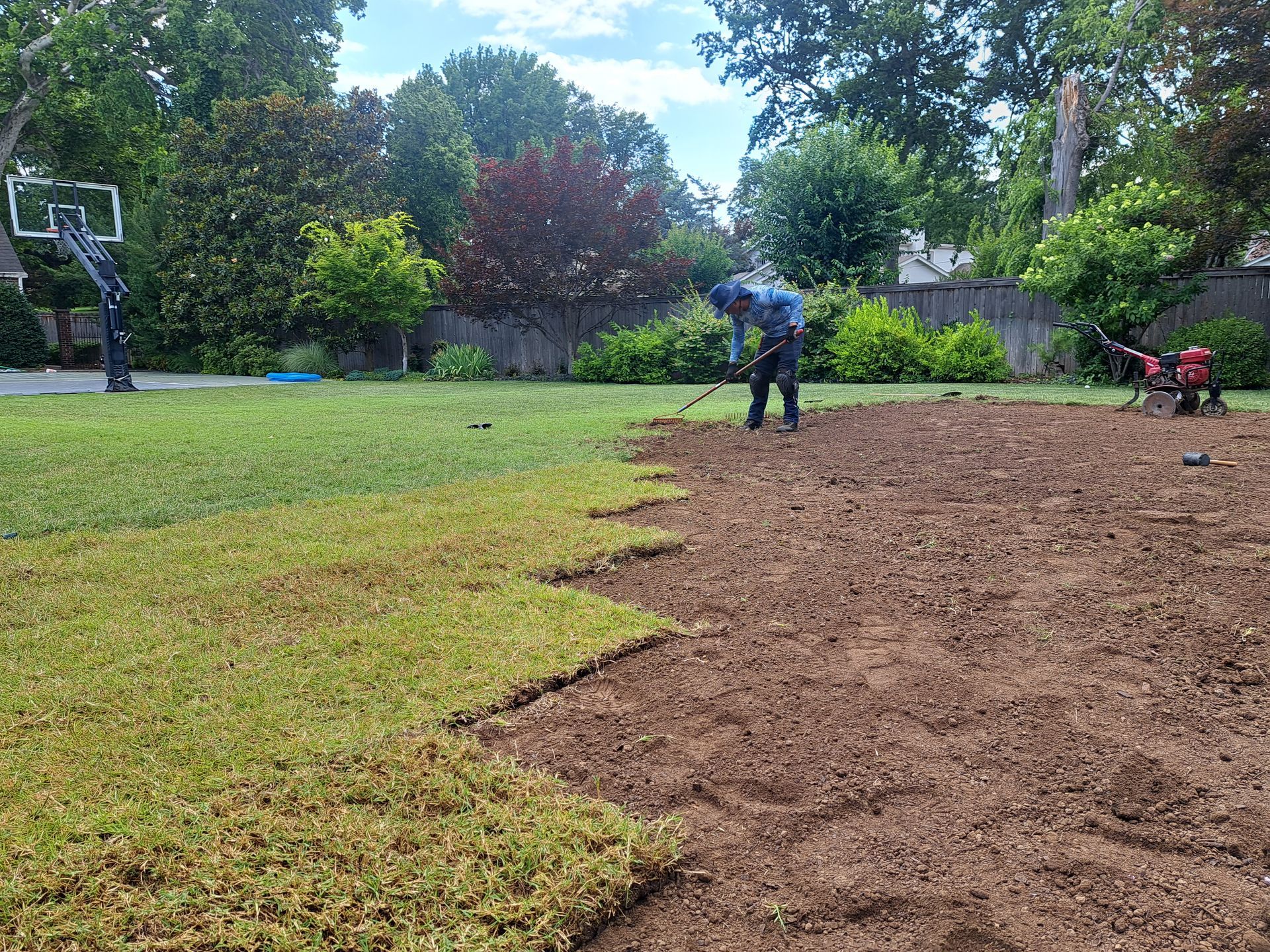 A man is working on a basketball court in a backyard.