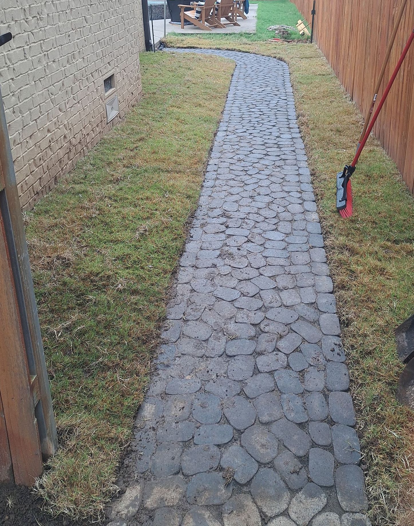 A stone walkway leading to a house with a mop in the grass.