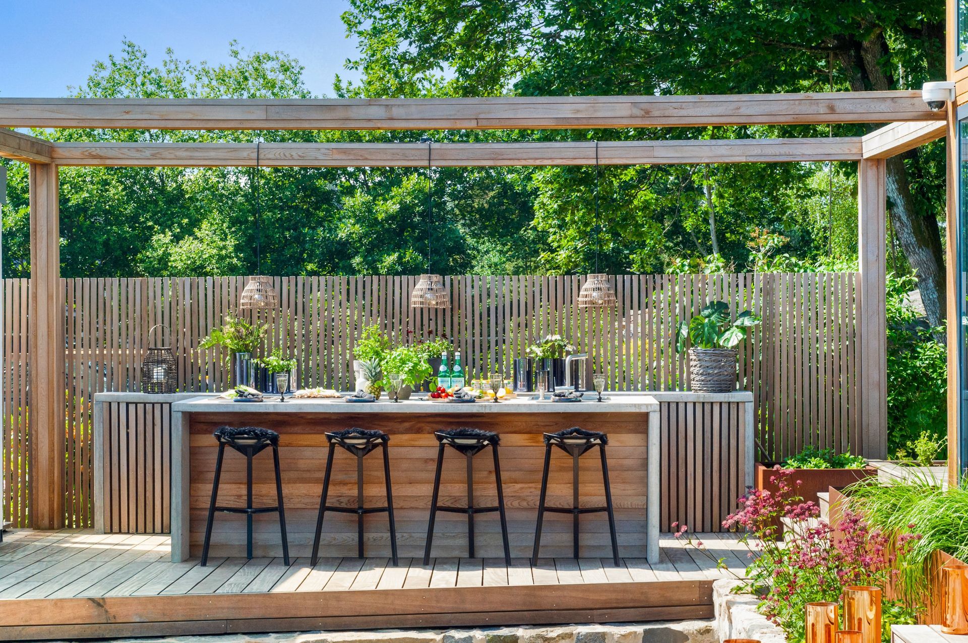 A wooden deck with a table and stools under a pergola.