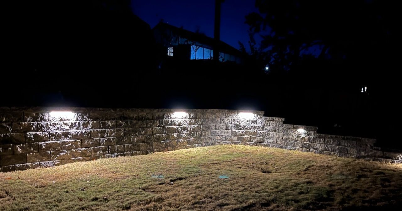 A stone wall with lights on it is lit up at night.