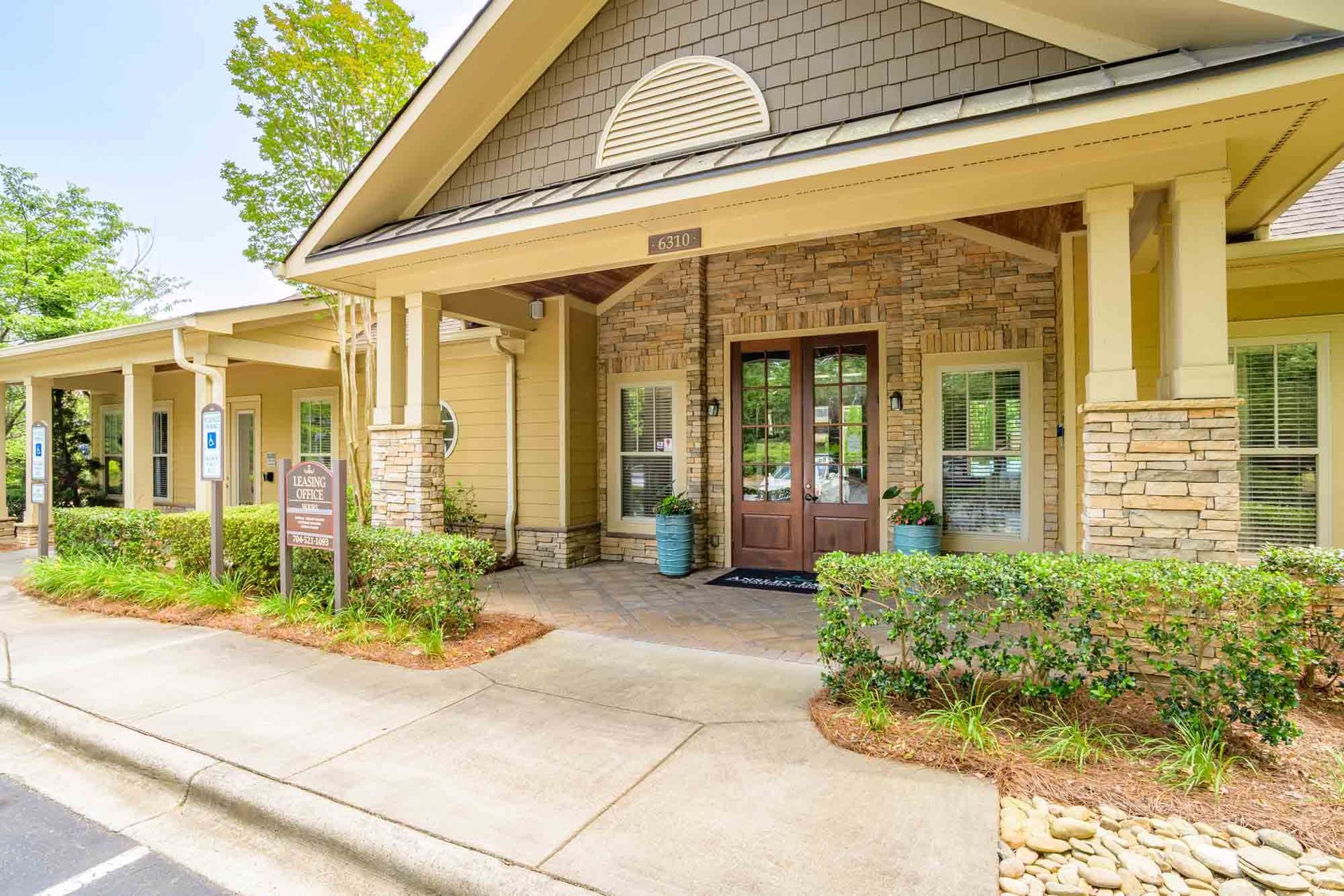 Exterior of a tan and brick building with columns, a brown door, and landscaping.
