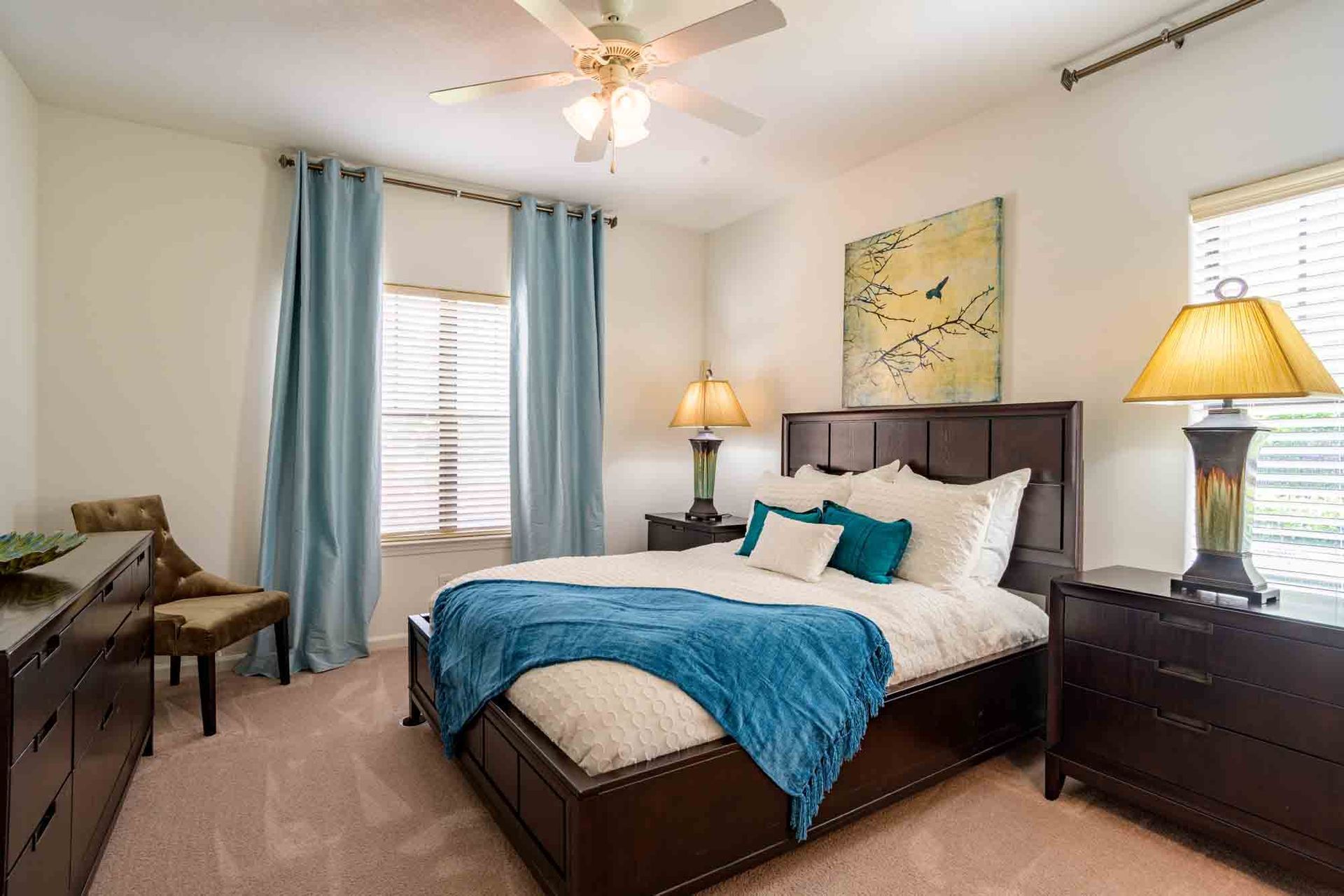 Bedroom with a dark bed frame, blue accents, lamps, and light-colored walls and carpet.