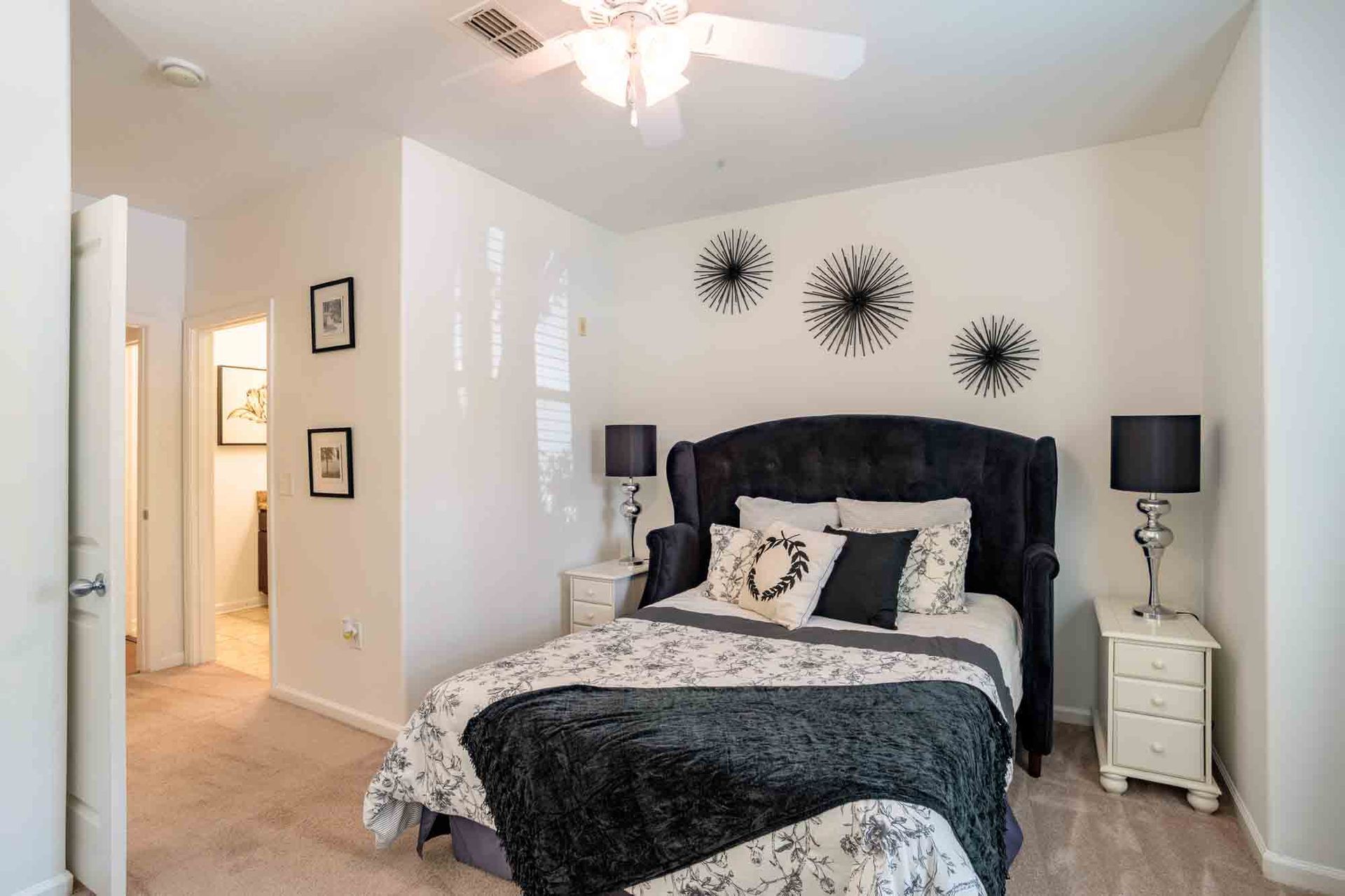 Bedroom with a black bed, white nightstands, and starburst wall decor; neutral colors.