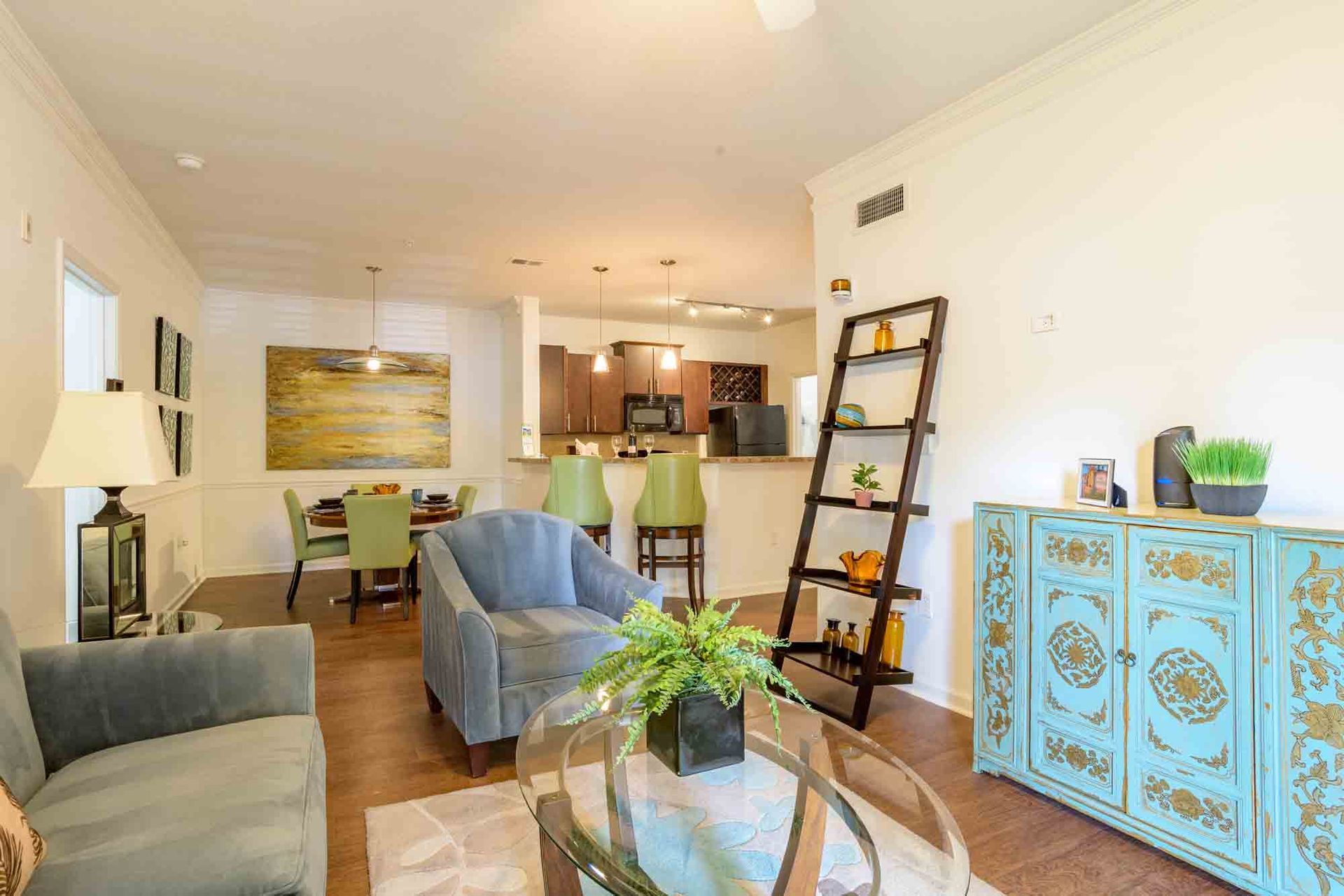 Living room with blue sofa and chair, wooden shelves, dining area, and kitchen.