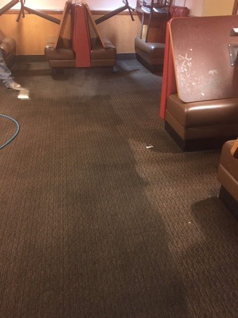 A man is cleaning the floor of a restaurant with a hose