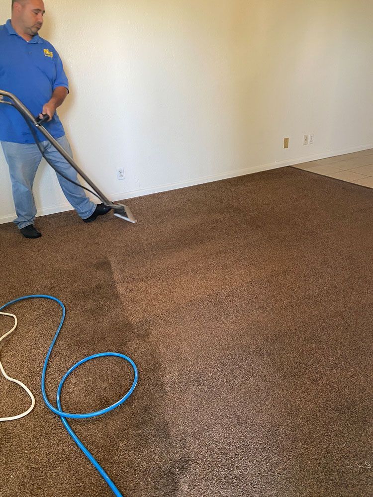 A man is cleaning a brown carpet with a vacuum cleaner.