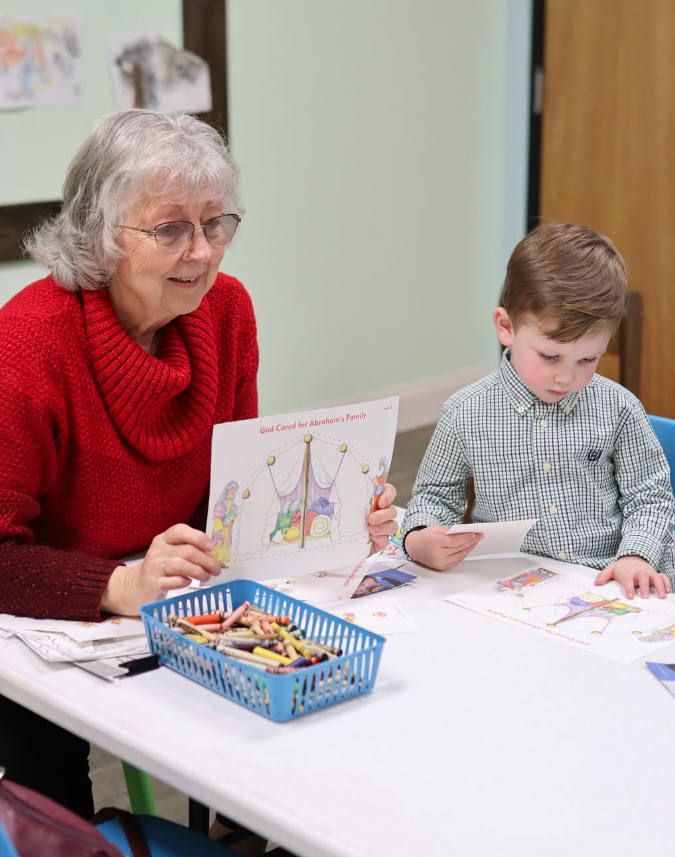 A woman and a boy are sitting at a table with a basket of crayons.