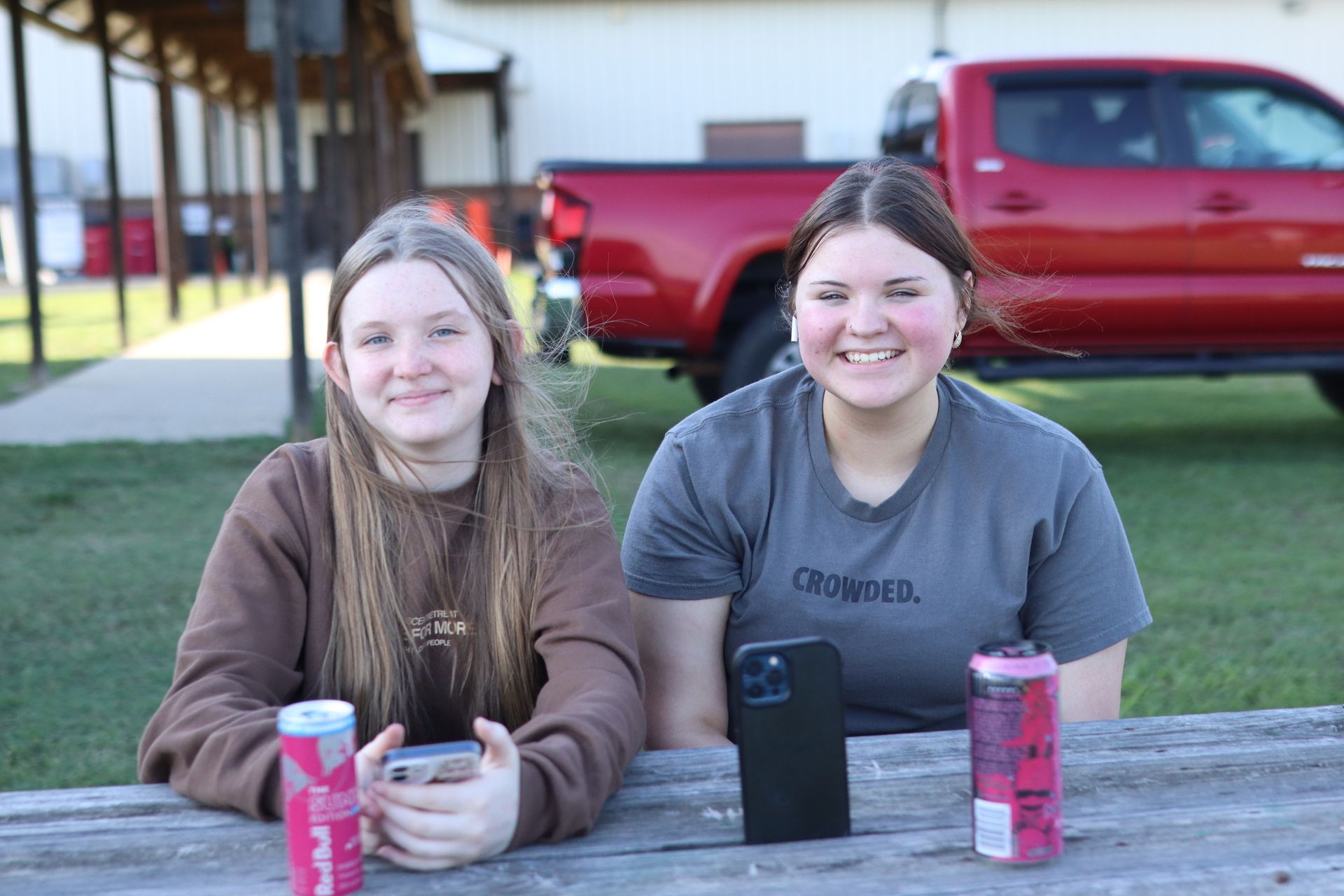 Two girls are sitting at a picnic table with a red truck in the background.