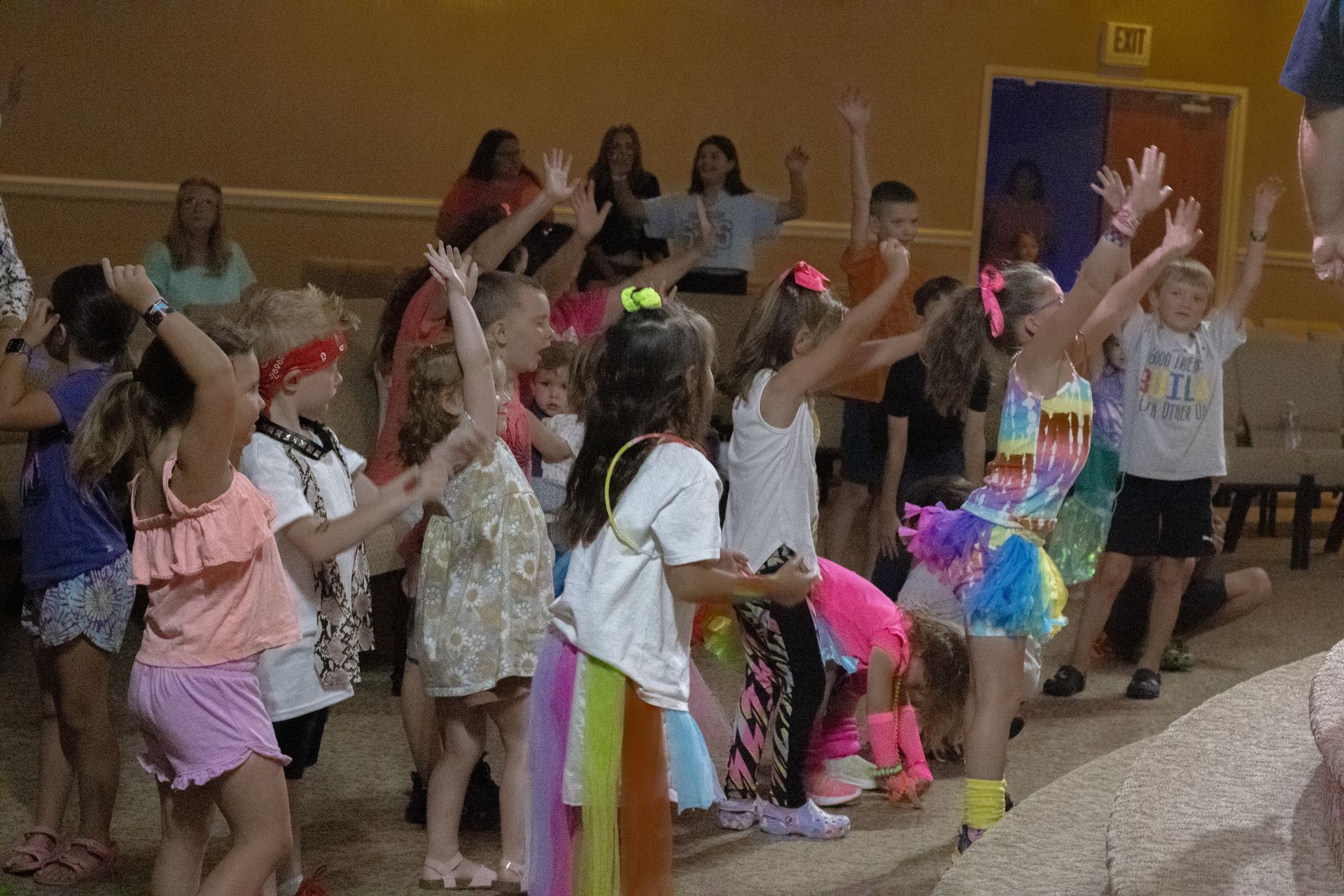 A group of children are dancing in a room with their hands in the air.