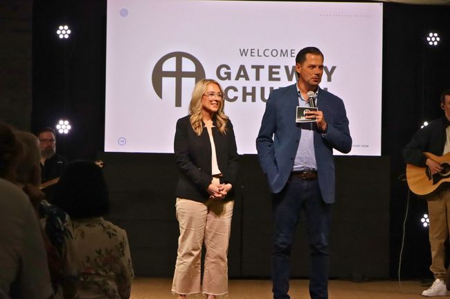 A man and a woman are standing in front of a screen that says welcome gateway church.