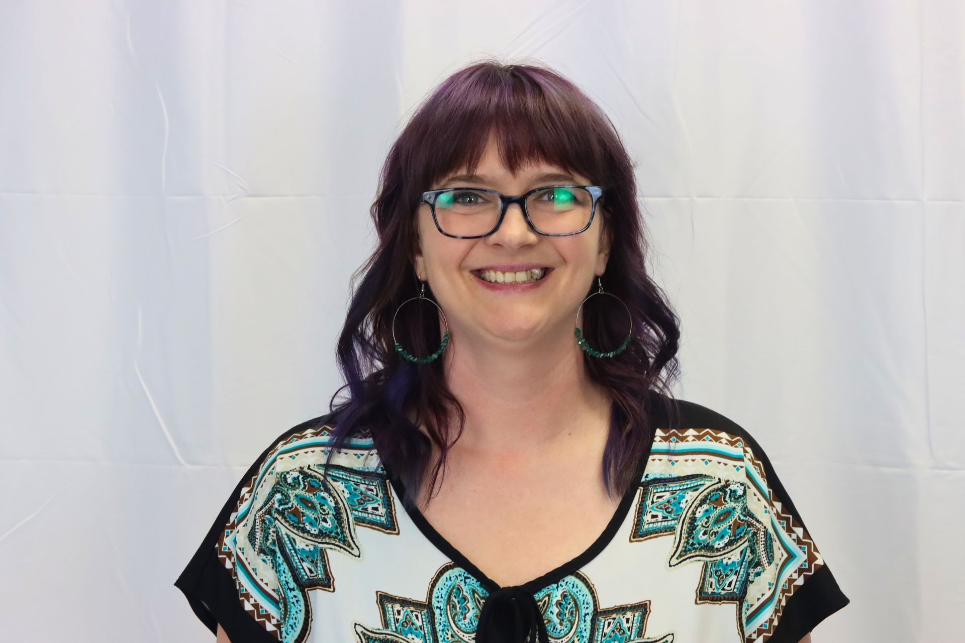 A woman with purple hair and glasses is smiling for the camera.