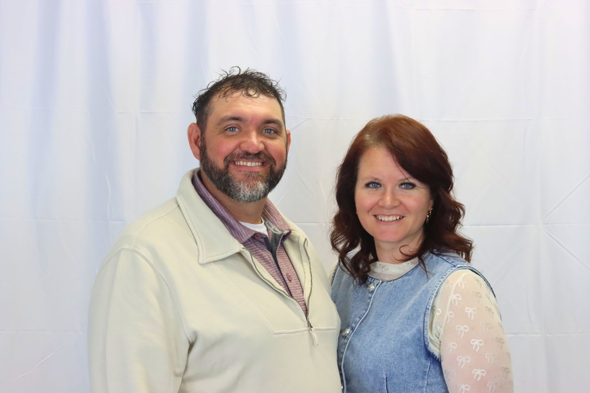 A man and a woman are posing for a picture in front of a white curtain.