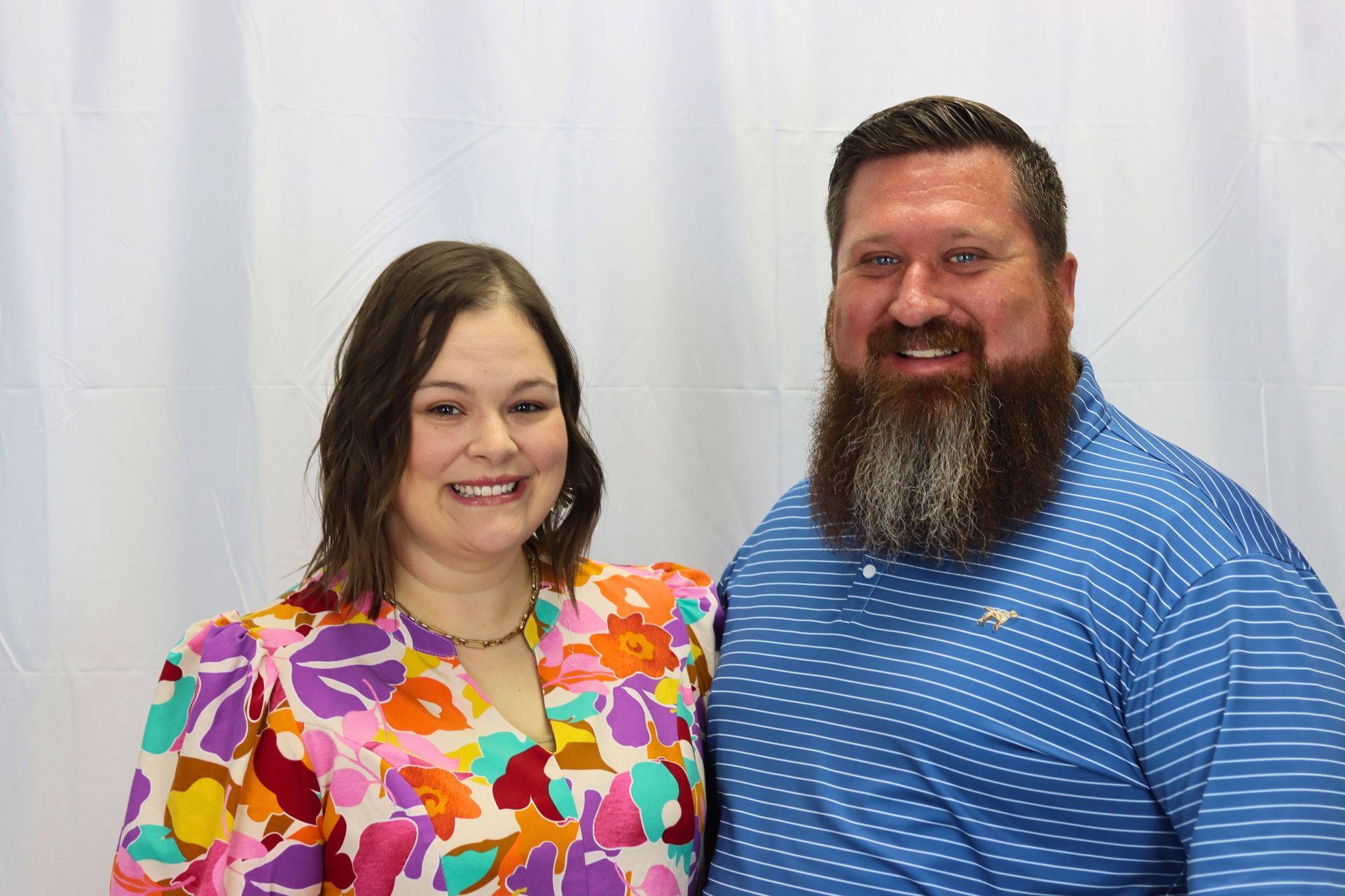A man with a beard and a woman in a floral shirt are posing for a picture.