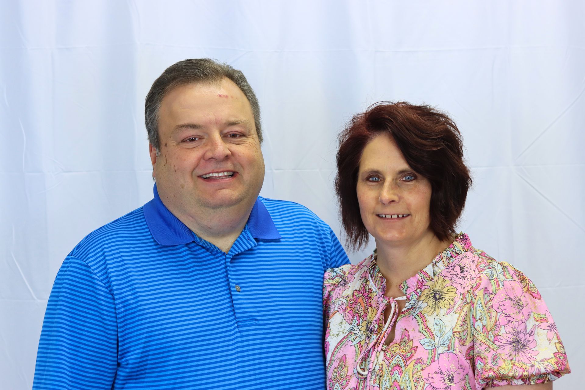 A man and a woman are posing for a picture in front of a white background.