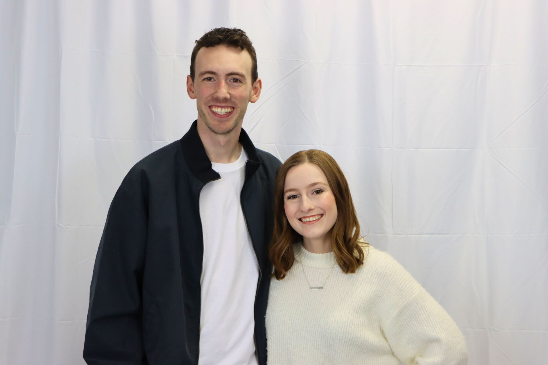 A man and a woman are posing for a picture in front of a white curtain.