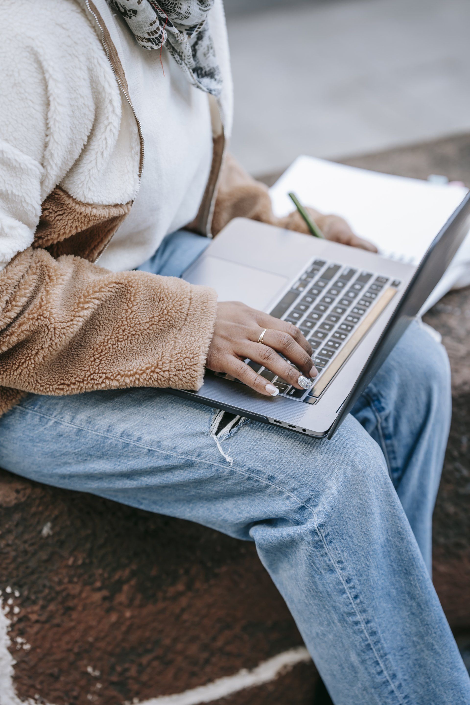 A woman is sitting on a brick wall using a laptop computer.