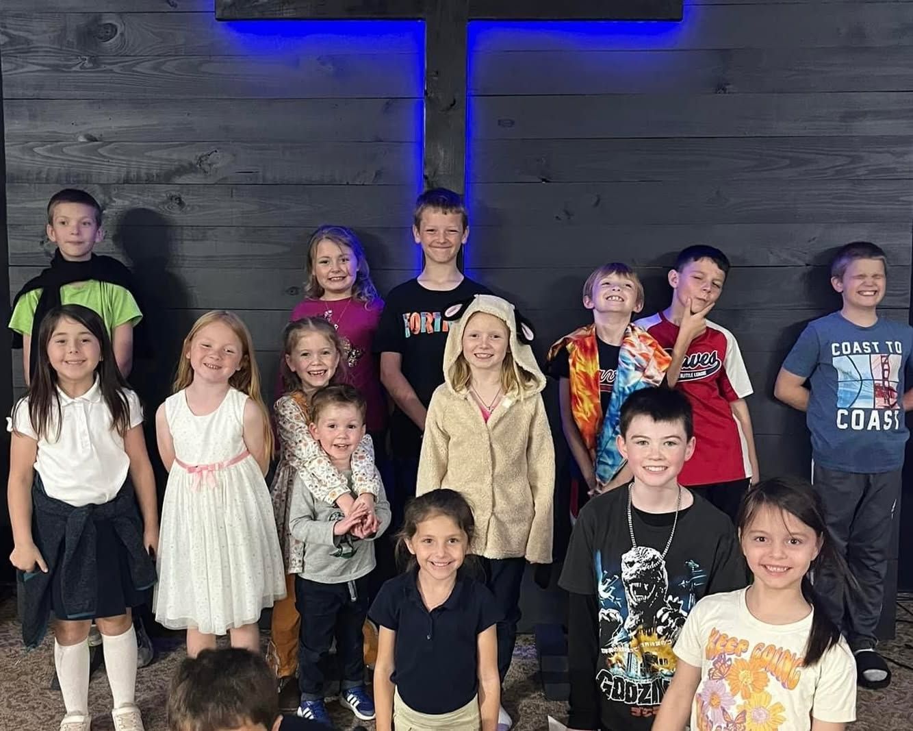 A group of children are posing for a picture in front of a cross.