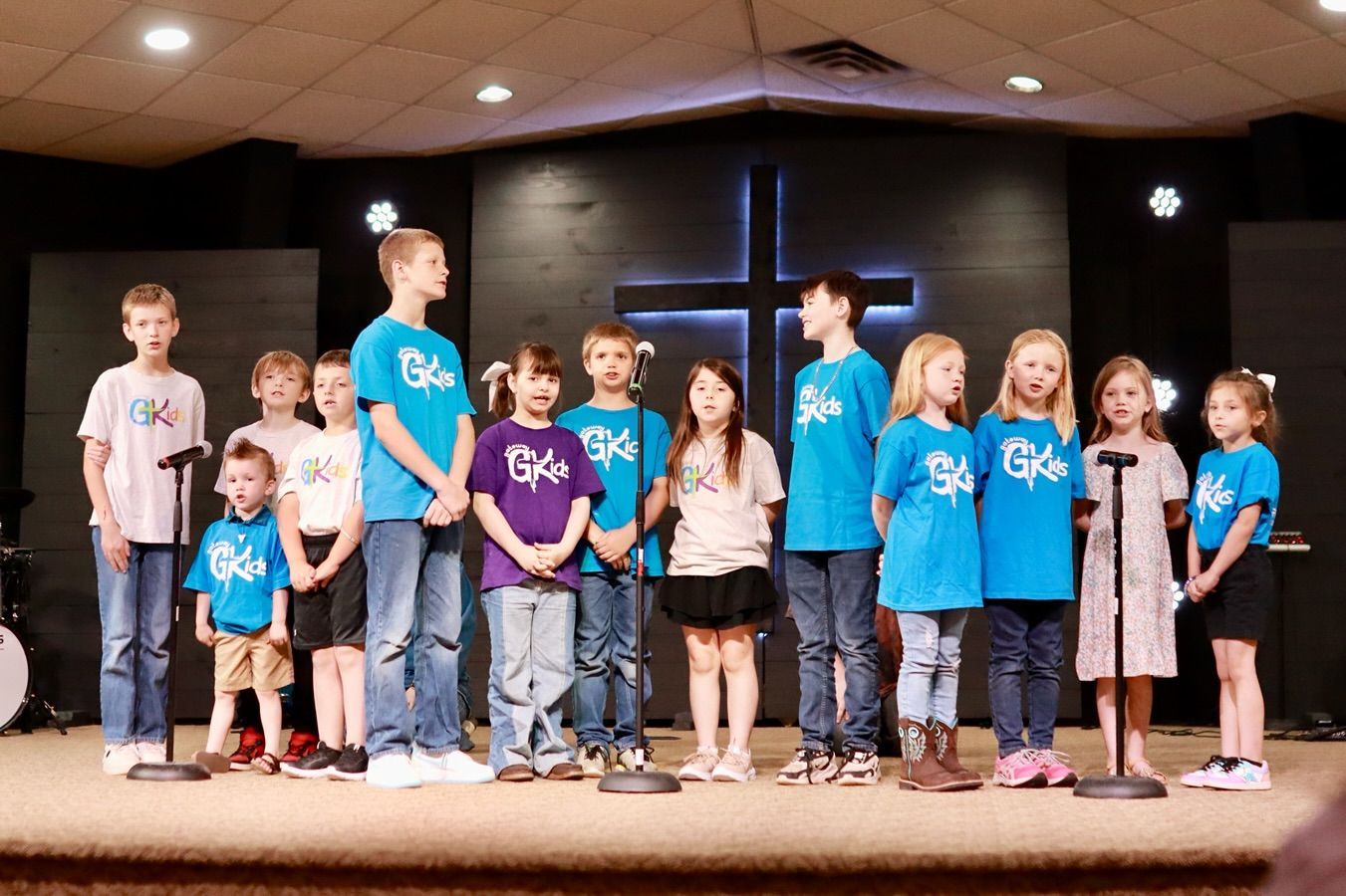 A group of children are standing in front of microphones on a stage.