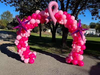 A pink balloon arch with a pink ribbon on it