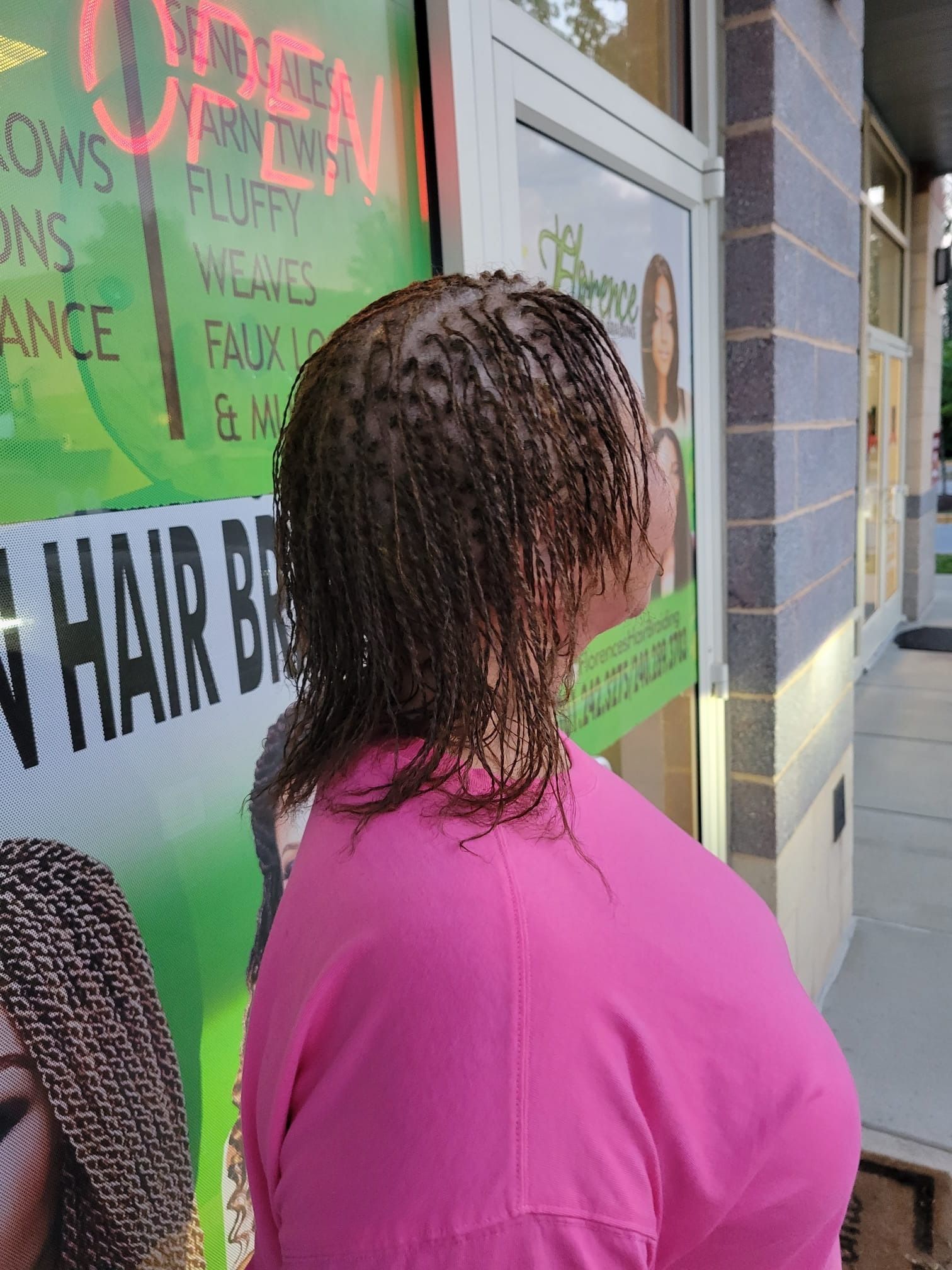 A woman with braids in her hair is standing in front of a hair salon.