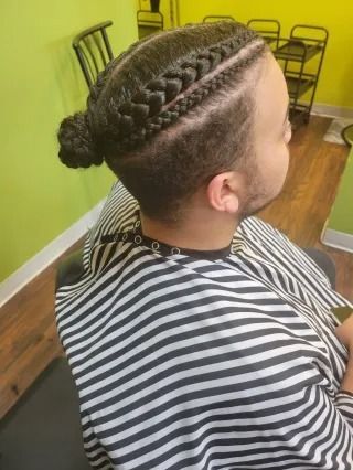 A man is getting his hair braided in a bun.