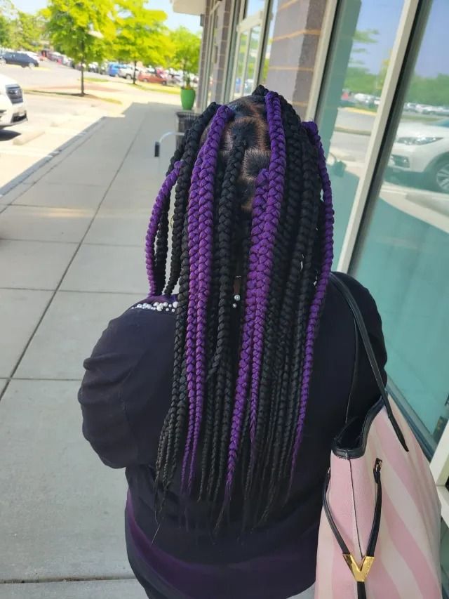 A woman with black and purple braids is standing on a sidewalk.