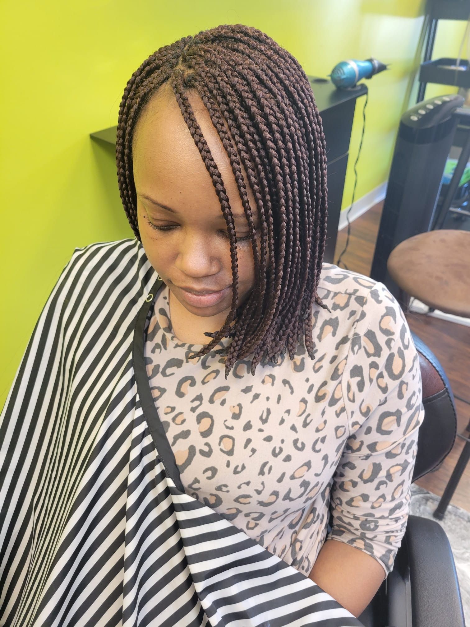 A woman with braids is sitting in a chair wearing a leopard print shirt.