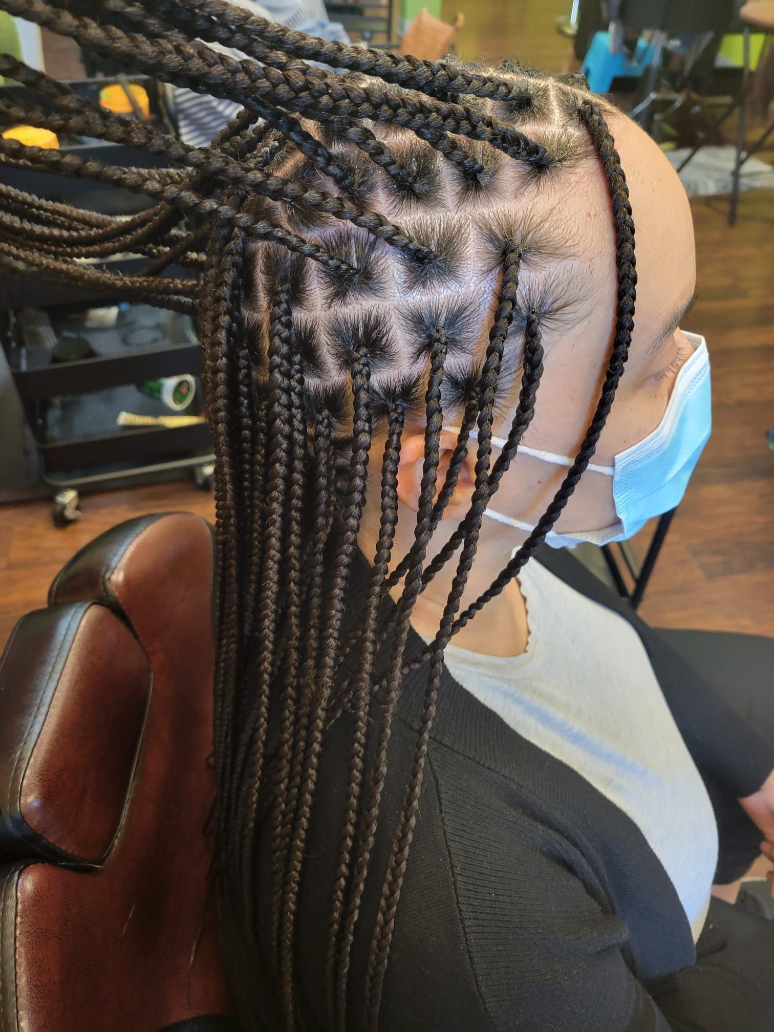 A woman wearing a mask and braids is sitting in a chair.