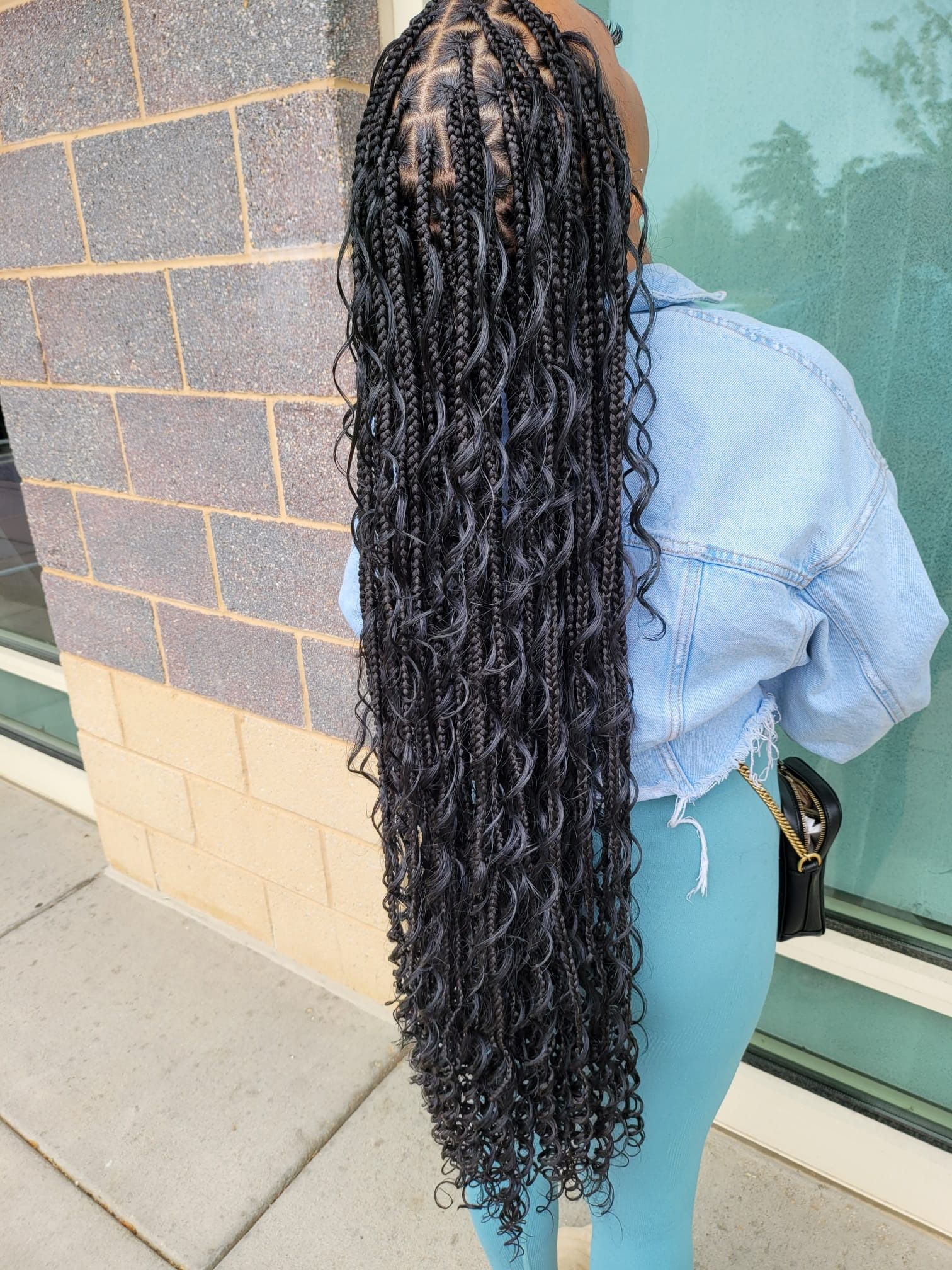 A woman with very long braids is standing in front of a brick building.