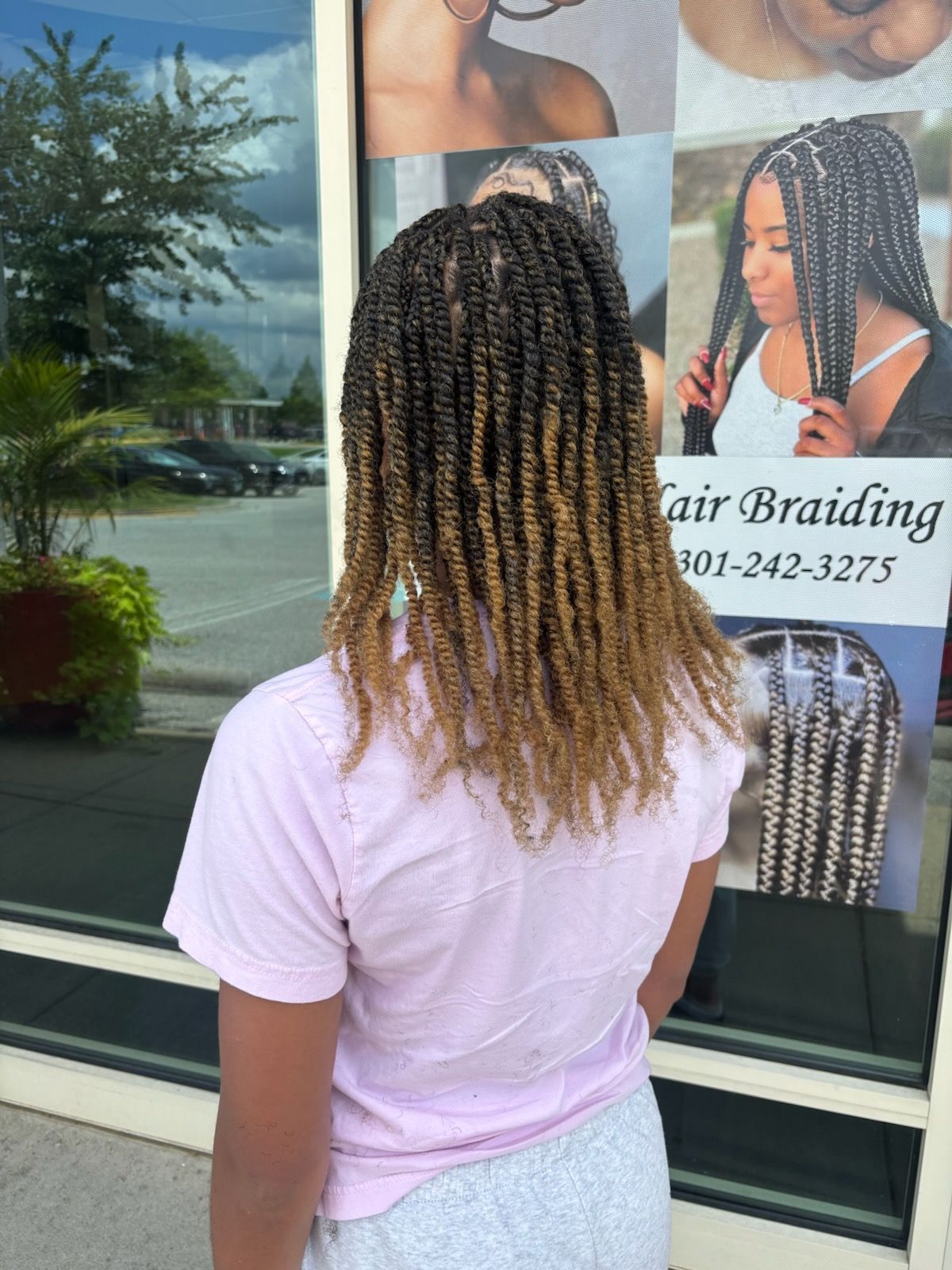 Woman with two-tone braids stands outside a hair braiding salon.