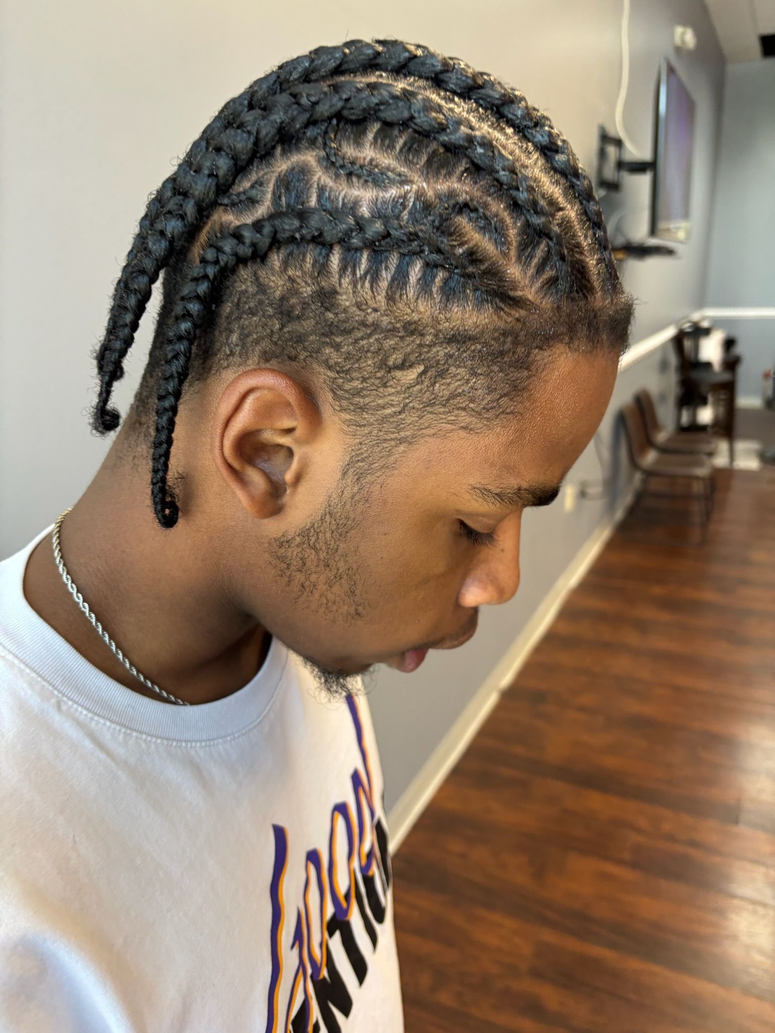 Man with braided hair and faded sides, wearing a white graphic t-shirt. Indoors.