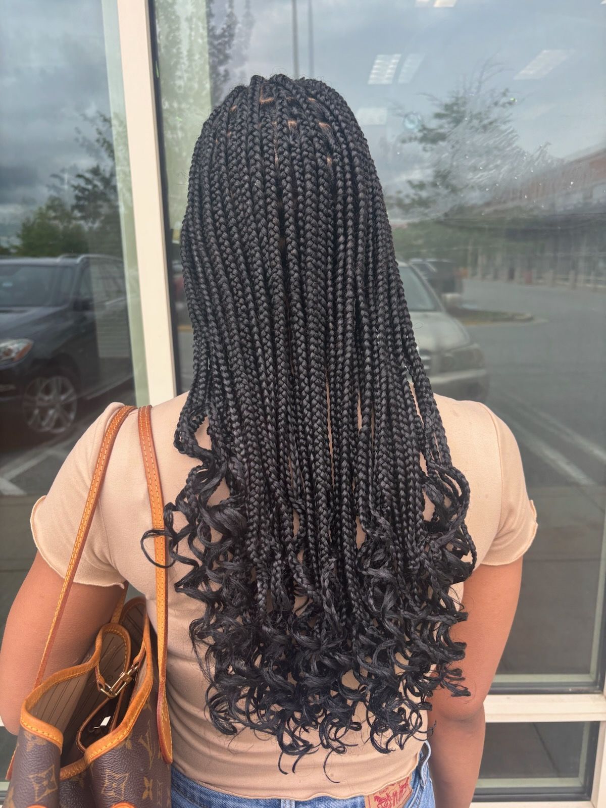 Woman with long black box braids featuring curled ends, standing outdoors.