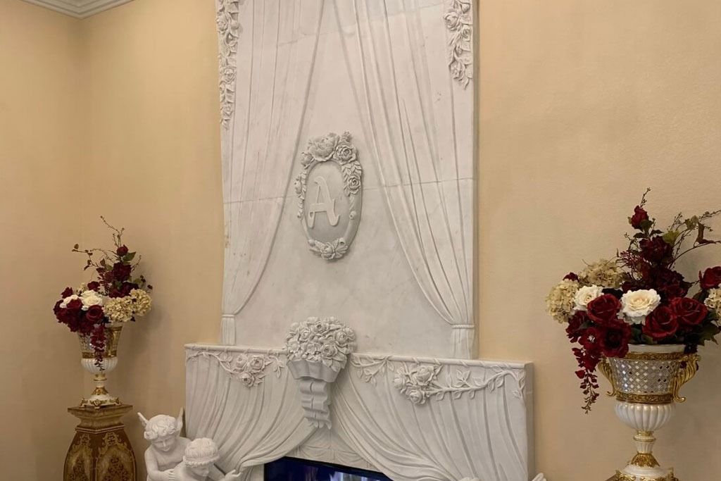 White decorative fireplace with floral arrangements on either side, against a beige wall.