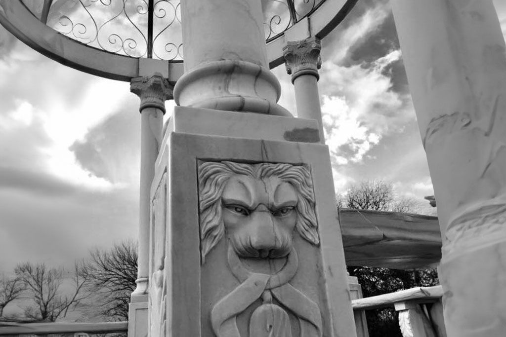 Stone pillar with carved lion face in a gazebo setting; cloudy sky in the background.