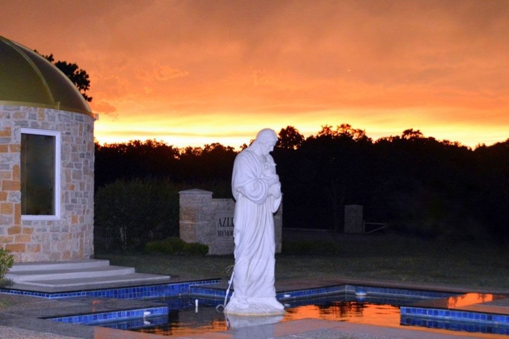 Statue of Jesus in front of a building with a golden dome and a sunset.