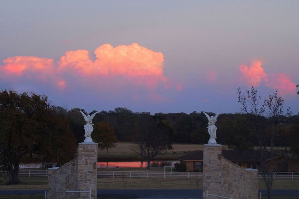 Two angel statues frame a landscape with pink-hued clouds at dusk.