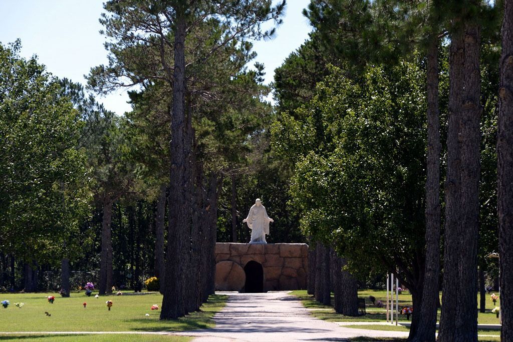 Path leading to a statue of Jesus in a cemetery, lined with trees and graves.