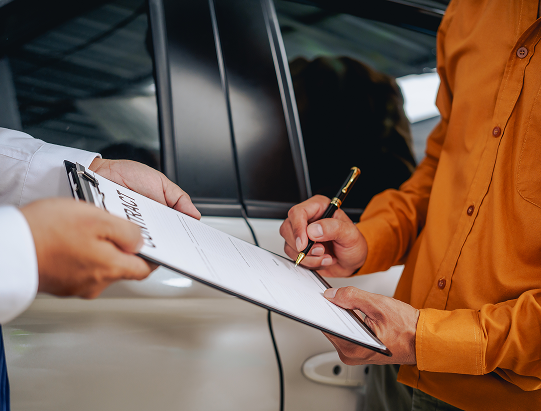 Man signing clipboard with car in background | Itasca Automotive