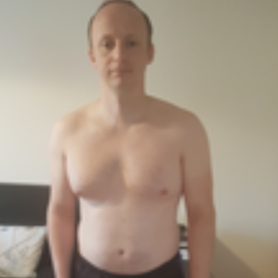 Man shirtless, standing against a neutral wall.