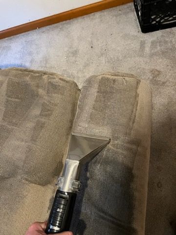 A person is cleaning an office chair with a vacuum cleaner.