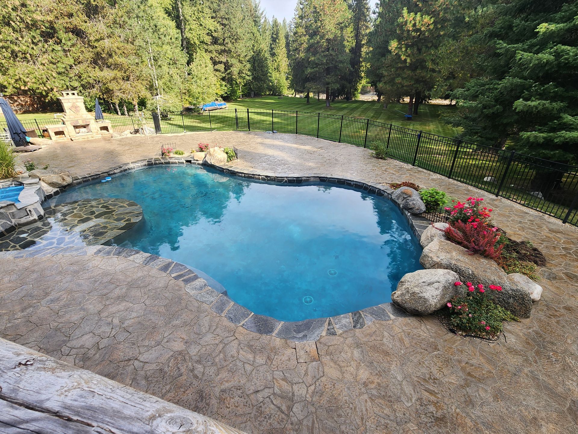 Heart-shaped pool with blue water, surrounded by rocks and plants, set in a grassy yard with trees.