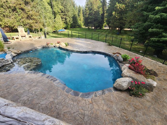Heart-shaped pool with blue water, surrounded by rocks and plants, set in a grassy yard with trees.