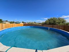 Above-ground pool filled with blue water under a bright blue sky, surrounded by a wooden fence.