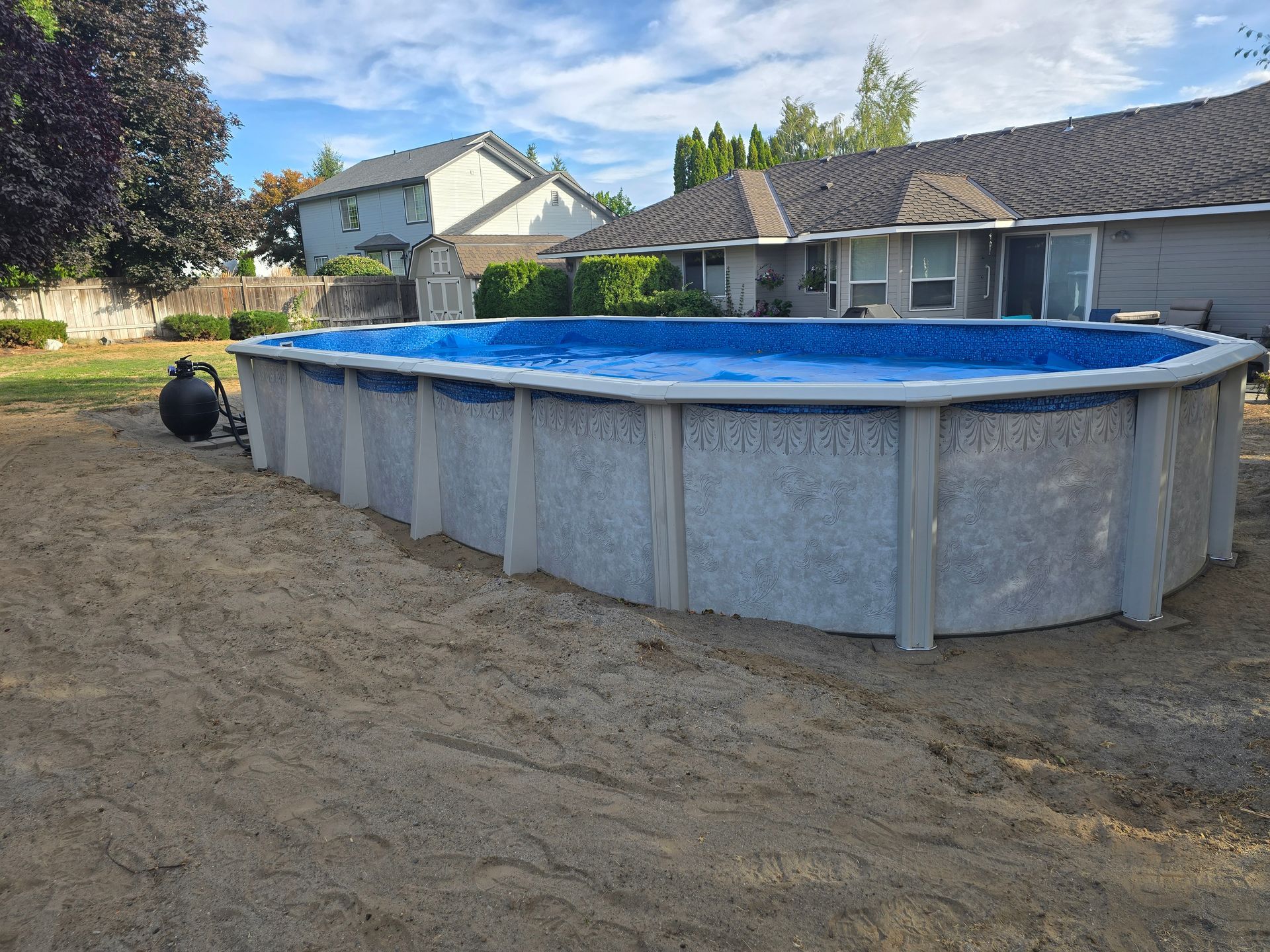 Oval above-ground pool in a backyard with a house in the background, blue water, and gray panel sides.